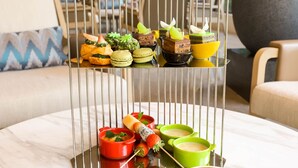 Een schaal met diverse gebakjes en desserts op een tafel, samen met een kop koffie met latte-art.