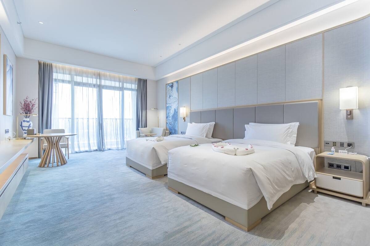 Een moderne hotelkamer met twee bedden, een zithoek en een groot raam met gordijnen.