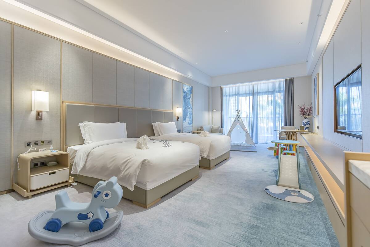 Een moderne hotelkamer met twee bedden, een bureau en een speelhoek.