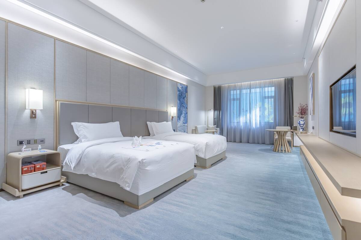 Een moderne hotelkamer met twee bedden, een bureau en een groot raam met gordijnen.