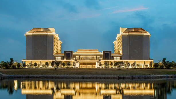 Een groot hotel met een symmetrische gevel, een centrale ingang en een reflectie in het water ervoor.