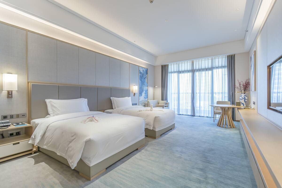 Een moderne hotelkamer met twee bedden, een bureau en een groot raam.