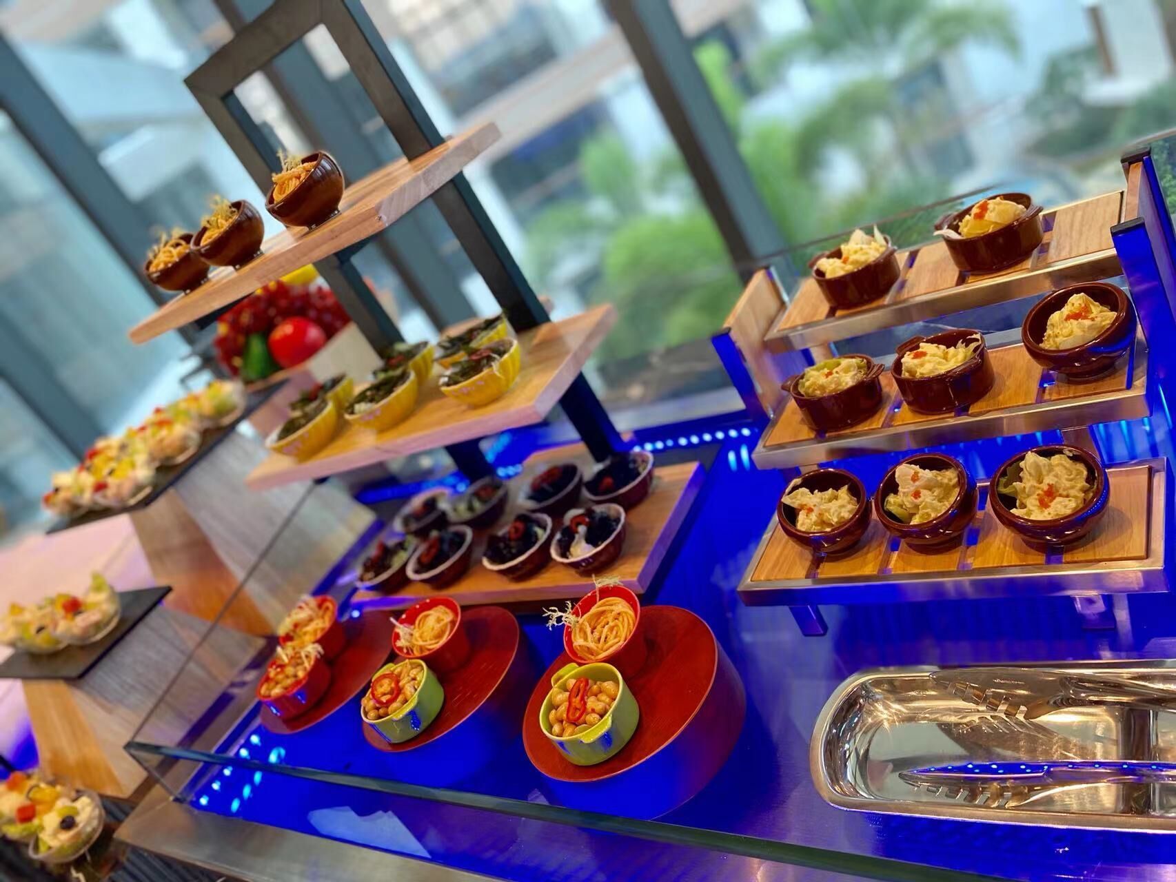 Variedad de postres expuestos en bases escalonadas dentro de una vitrina, con vistas al exterior y vegetación.