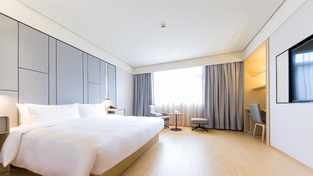A modern hotel room with a large bed, a desk, a chair, and a window with curtains. - Ji Hotel (Shanghai)