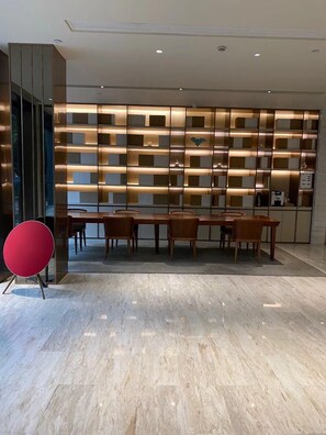 Un interior moderno con comedor, una silla roja, una pared con estanterías e iluminación empotrada en el techo.