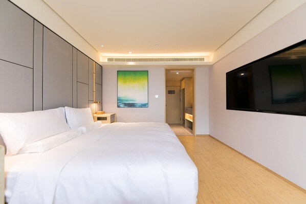 Habitación de hotel moderna con una cama grande, un televisor de pantalla plana, un cuadro en la pared y un vestidor.