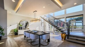 A modern kitchen with a dining area, a staircase, and large windows.