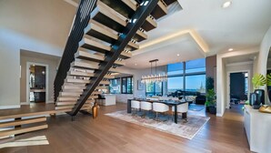 A modern interior with a wooden staircase, a dining area, and large windows offering a view.