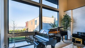 A modern living room with a grand piano, a television, and a large window overlooking a cityscape.