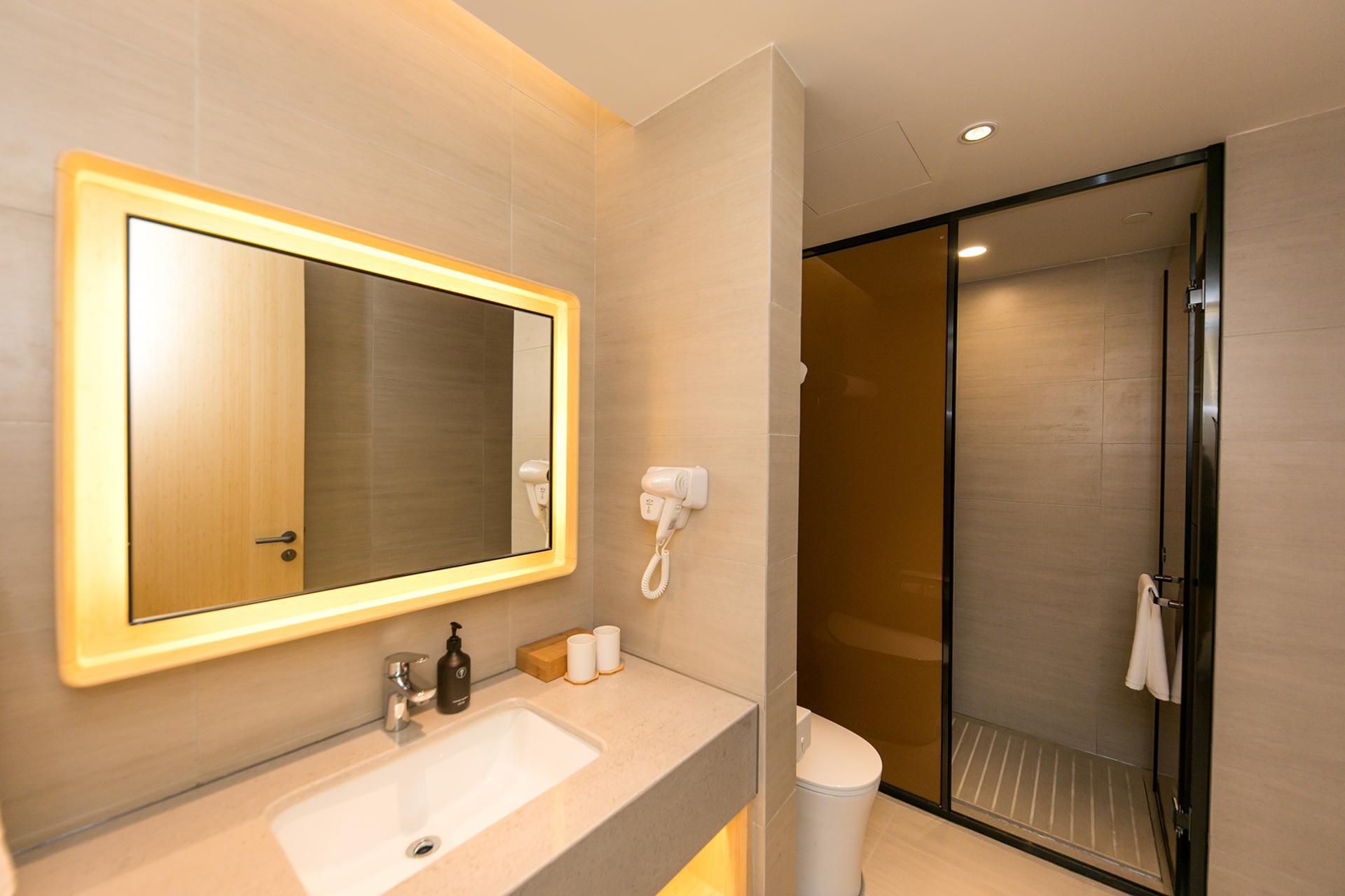 A modern bathroom with a large mirror, a sink, a handheld hair dryer, and a shower area.