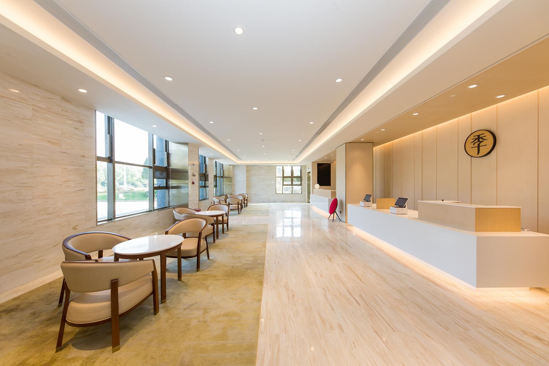 A modern hotel lobby with a reception desk, seating area, and large windows.