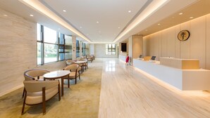 Un hall d’hôtel moderne avec un comptoir d’accueil, un espace salon et de grandes fenêtres.