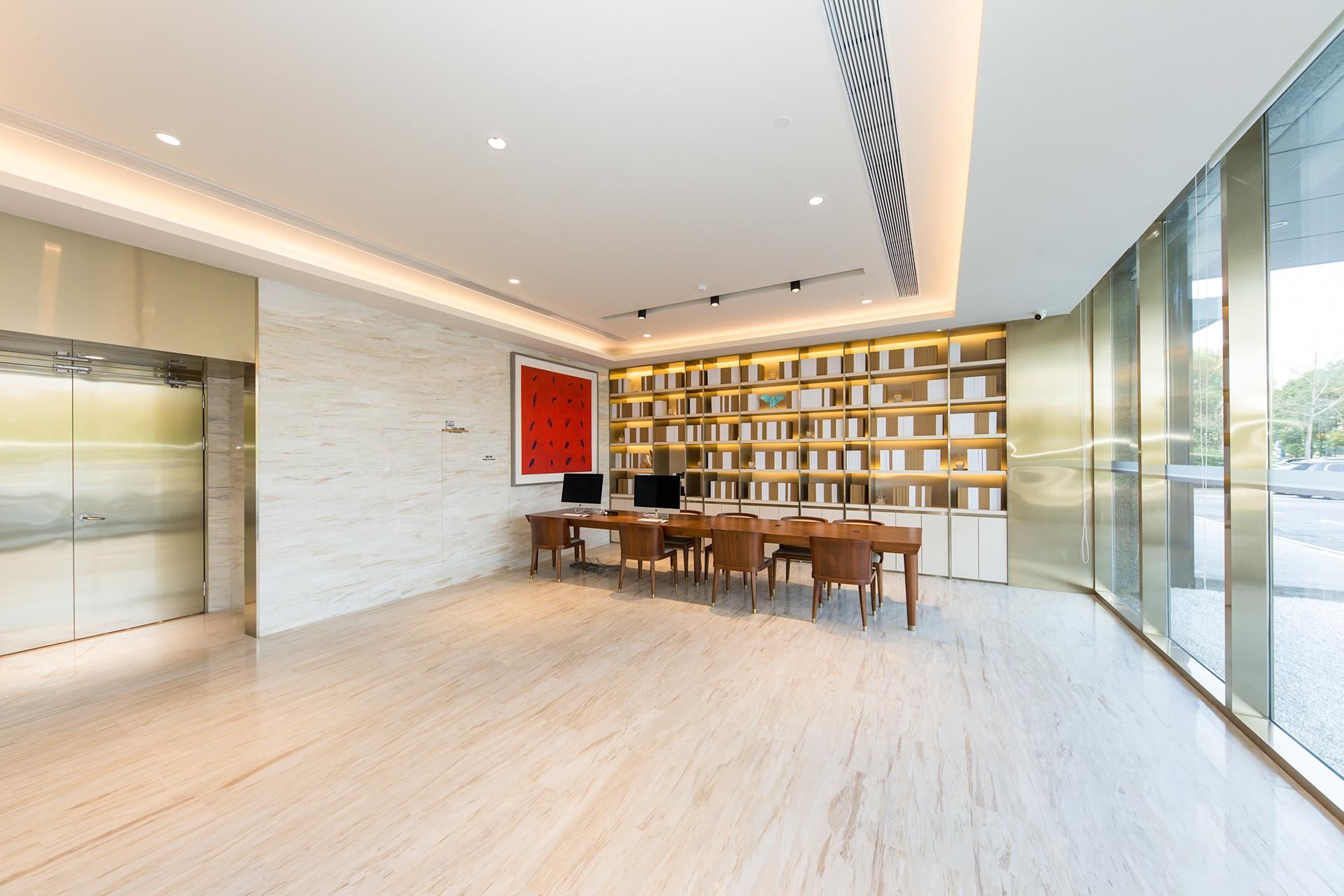 A modern interior with a wooden table and chairs, a large bookshelf, and a view through a glass wall.