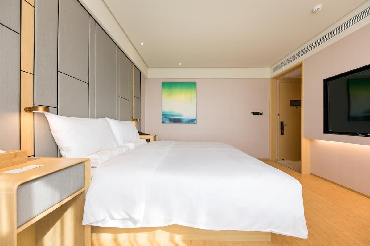 A hotel room with a bed, bedside tables, a TV, and a painting on the wall.