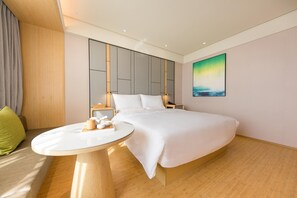 Et moderne hotelværelse med en stor seng, et sengebord, et lille bord med bakke, og et maleri på væggen.