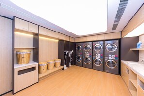 A laundry room with multiple washing machines, baskets, and a drying rack. - Ji Hotel (Nanjing)