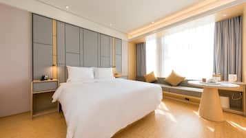 Quarto de hotel moderno com uma cama grande, mesas de cabeceira, uma mesa de pequeno-almoço redonda e uma área de estar com um sofá e almofadas.