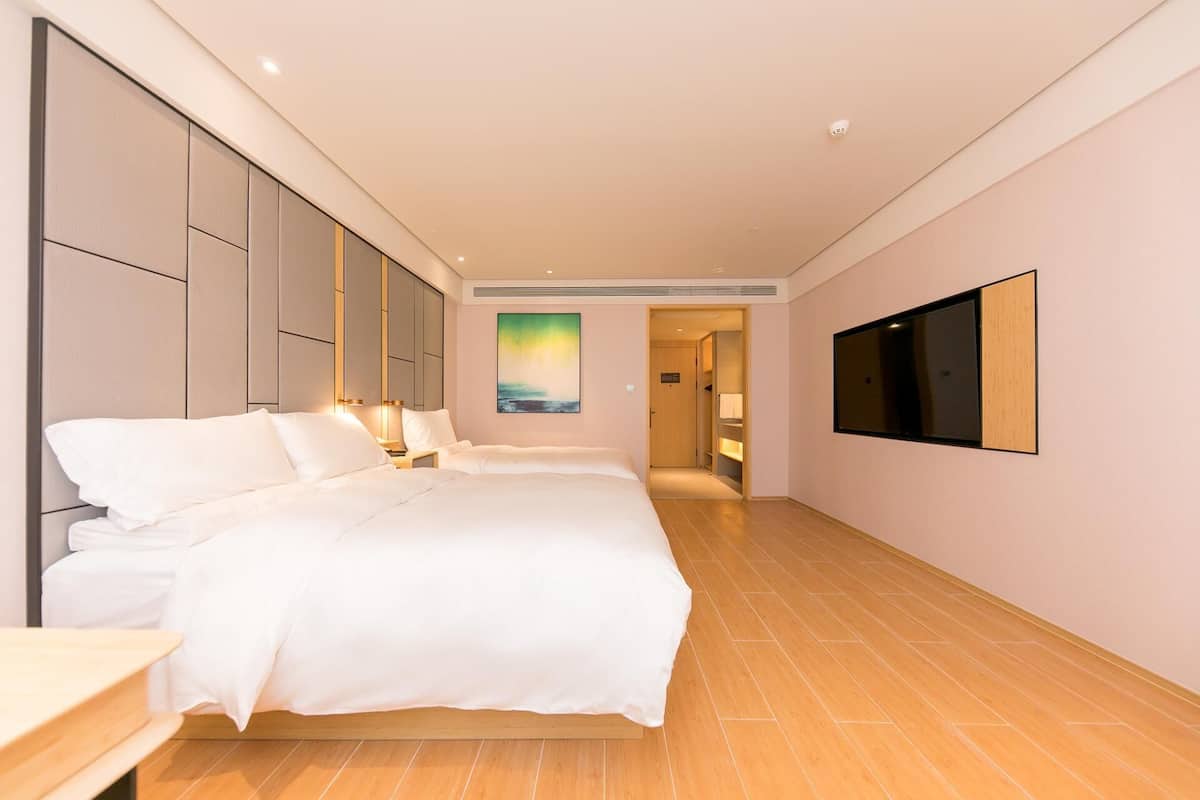 A hotel room with a large bed, a TV mounted on the wall, and a painting on the wall.