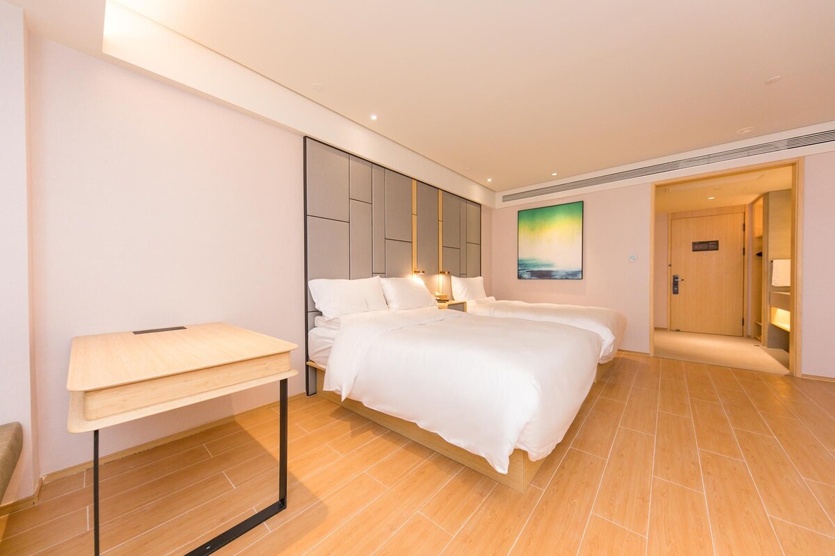 A hotel room with a bed, bedside tables, a desk, and a painting on the wall.