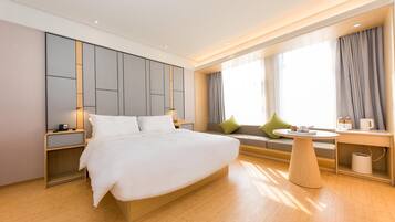 A modern hotel room with a large bed, a seating area with a table, and a window with curtains.