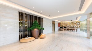 Un hall d’entrée moderne avec un sol en marbre, une grande plante en pot, un banc en bois et une bibliothèque.