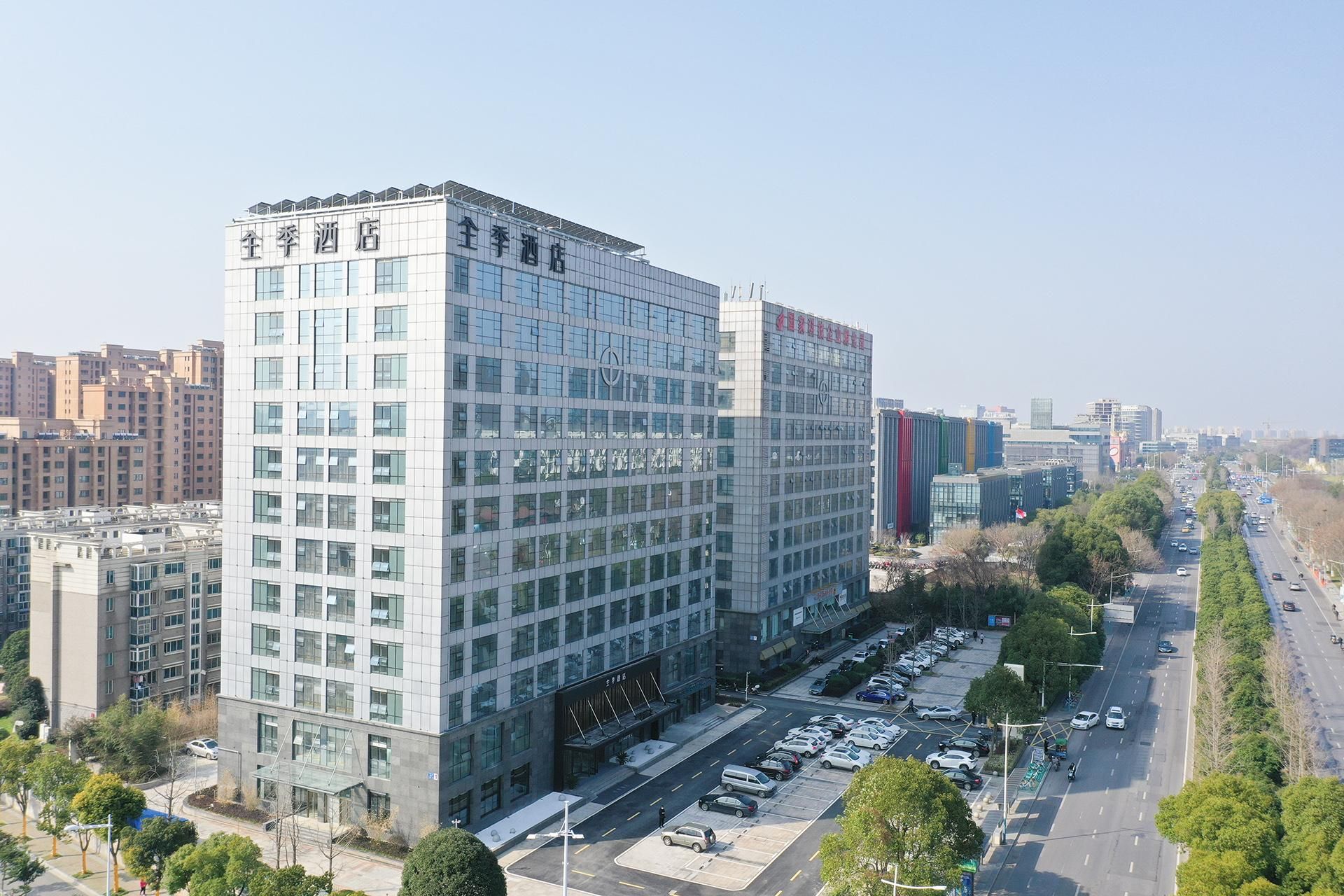 A modern hotel with a glass facade, multiple floors, and a parking lot.