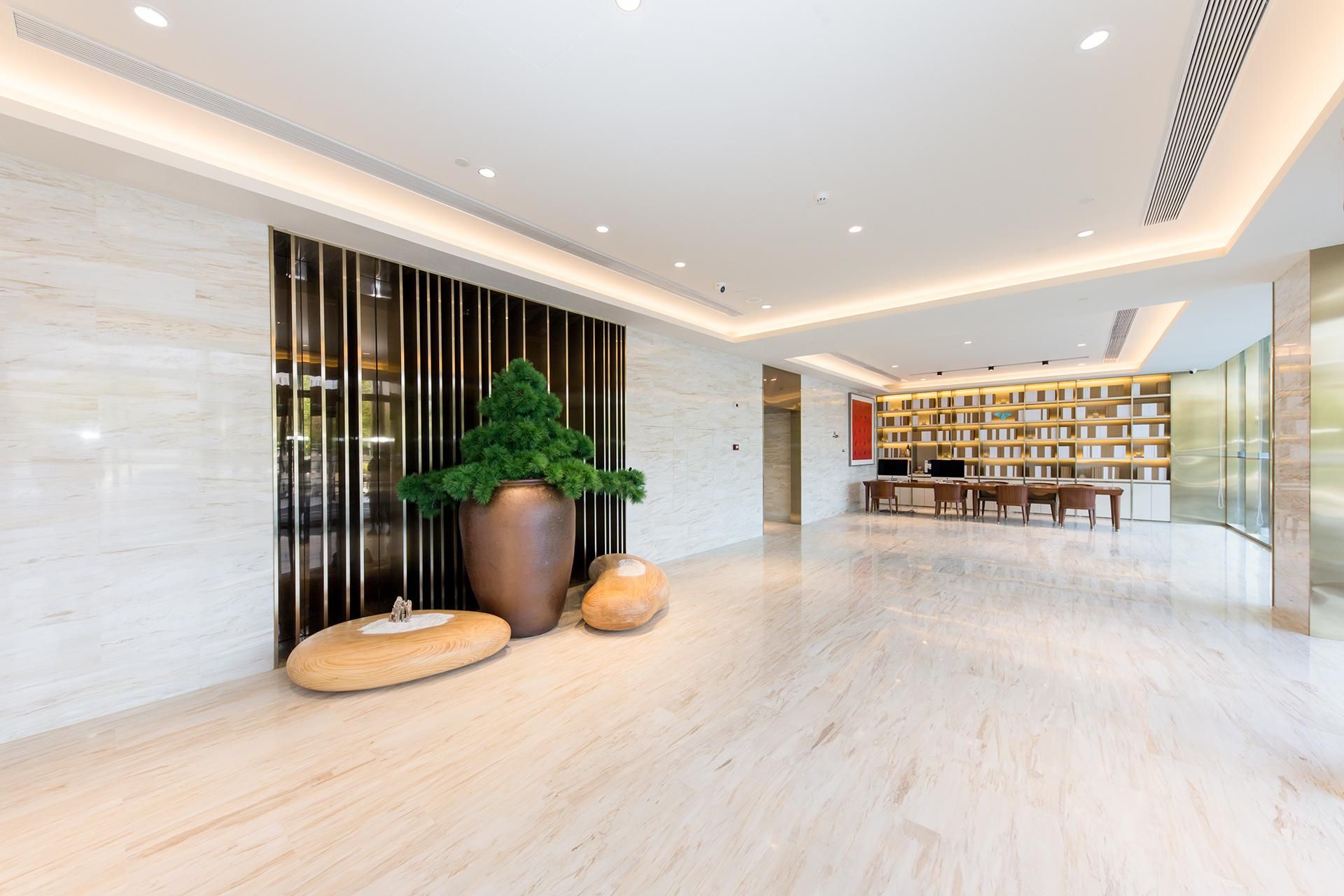 Eine moderne Lobby mit Marmorboden, einer großen Topfpflanze, einer Holzbank und einem Bücherregal.