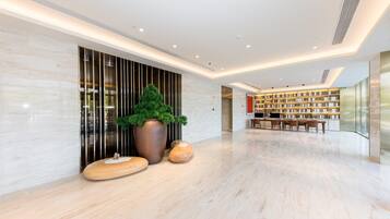 Eine moderne Lobby mit Marmorboden, einer großen Topfpflanze, einer Holzbank und einem Bücherregal.