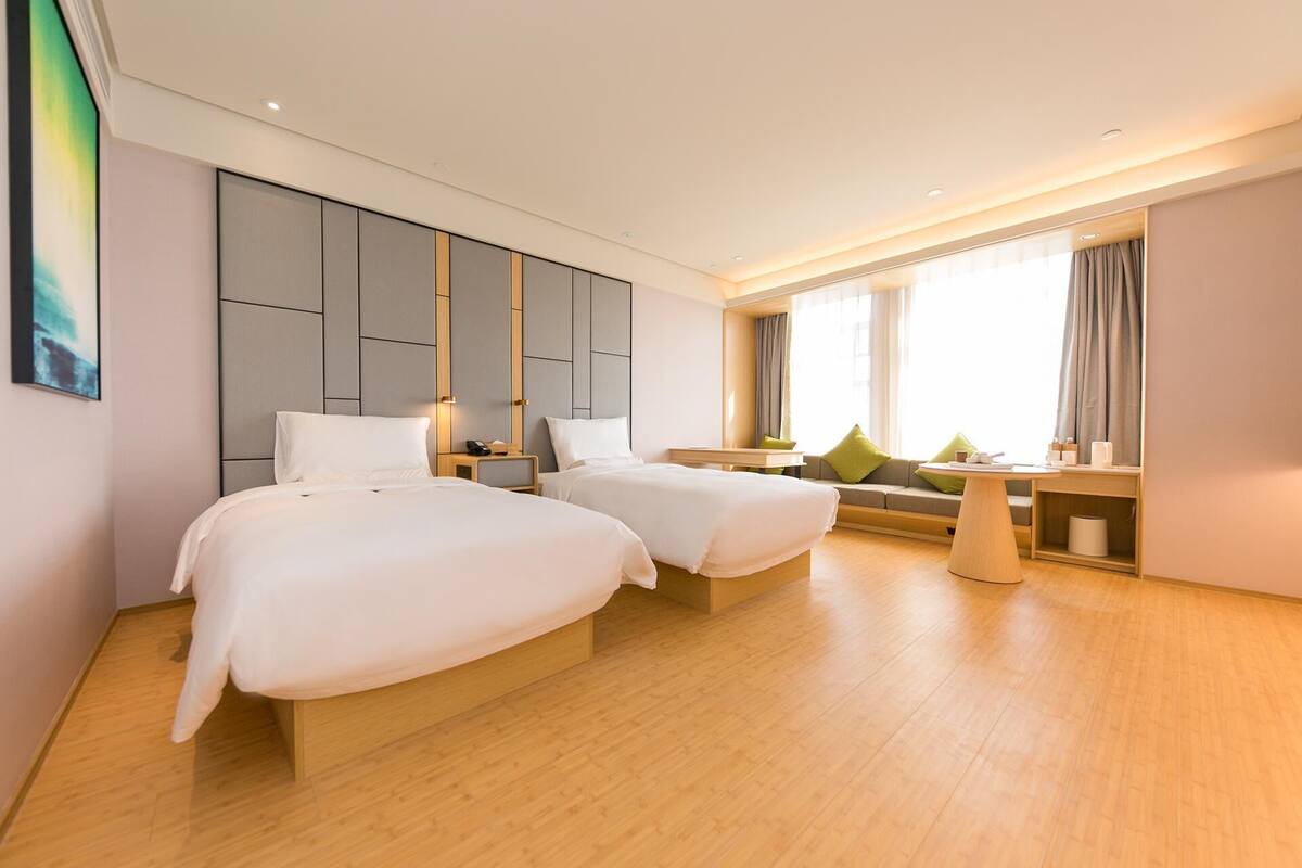 A hotel room with two beds, a sofa, a small table, and a large window with curtains.