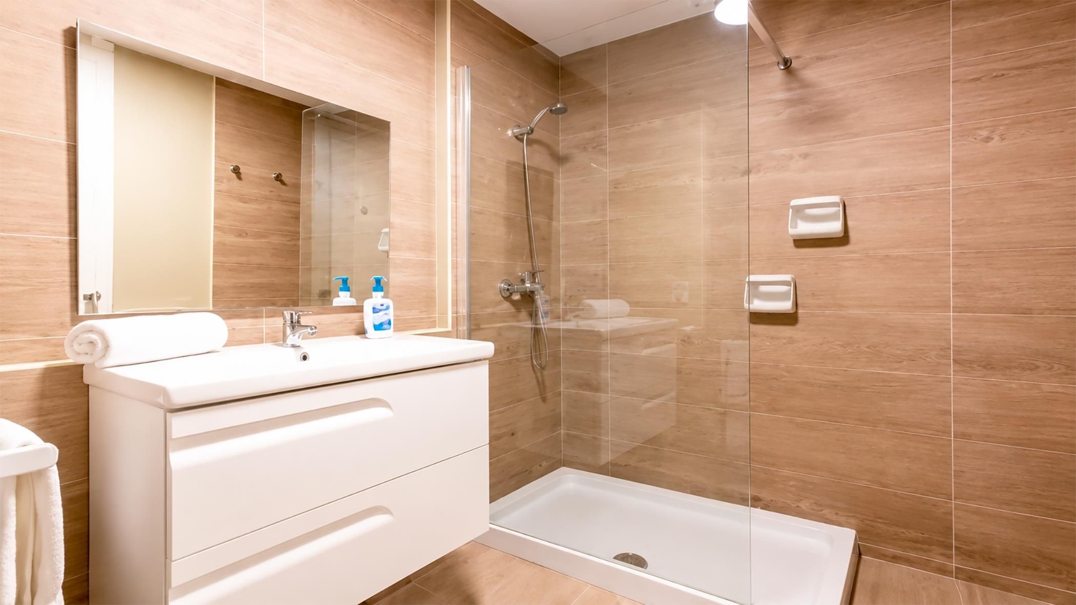 Um banheiro moderno com box de vidro, toucador branco com espelho e vaso sanitário.