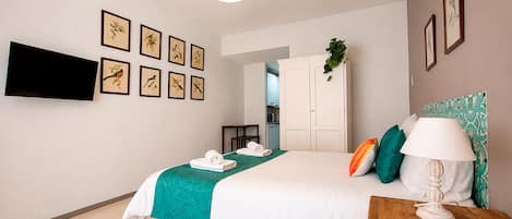 A hotel room with a bed, a TV mounted on the wall, and framed pictures.