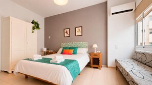 Une chambre à coucher avec un lit, des tables de chevet, un canapé, une armoire et une fenêtre.