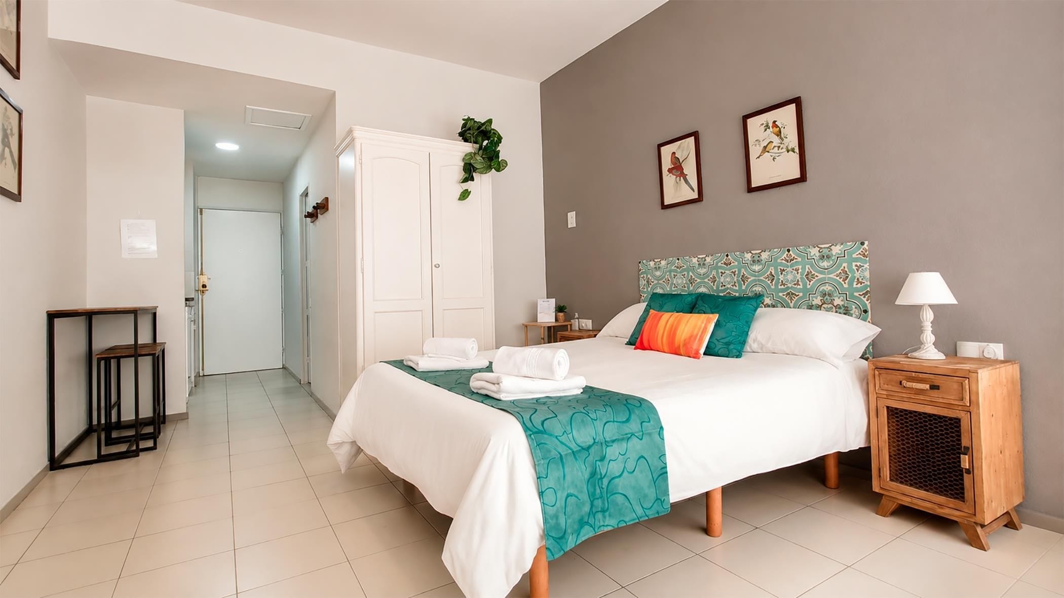 A hotel room with a bed, bedside tables, a wardrobe, and a view of the hallway.