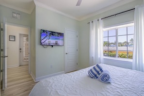 A bedroom with a bed, a television on the wall, a window with curtains, and a door. - Beach Club Cottage w/ Private Beach & Heated Pool (Sarasota)