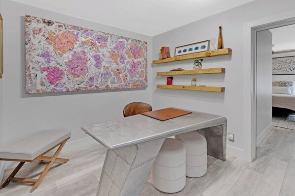 A modern room with a marble table, a large abstract painting, and wooden shelves with decorative items.