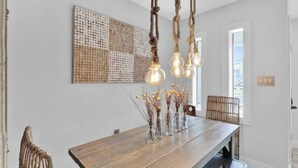 Un comedor con mesa de madera, lámparas colgantes y un adorno en la pared.
