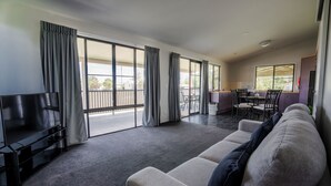 Una sala de estar moderna con un sofá, un televisor de pantalla plana y un balcón con ventanas amplias.