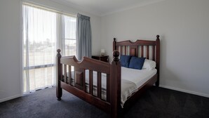 Un dormitorio con una cama de madera, una mesita de noche y vistas amplias a través de grandes ventanales.