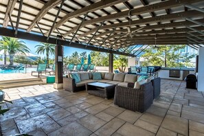 Ein überdachter Patio-Bereich im Freien mit Korbmöbeln, einem Pool und Blick auf Palmen.