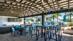 Un espace extérieur aménagé avec un patio, des sièges, une piscine et une zone couverte équipée d’un barbecue.