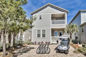 A two-story residential building with a balcony, a driveway with a golf cart, and bicycles parked in the front.