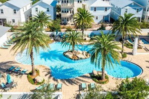 A swimming pool surrounded by palm trees, with lounge chairs and a view of residential buildings.
