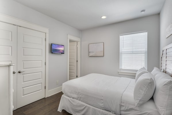 A bedroom with a bed, a television, a window with blinds, and a door.