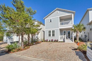 A two-story residential building with a front porch, a balcony on the upper floor, and a paved driveway.
