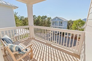 A wooden deck with a white railing, a wooden chair with striped cushions, and a view of a residential area with houses and trees.
