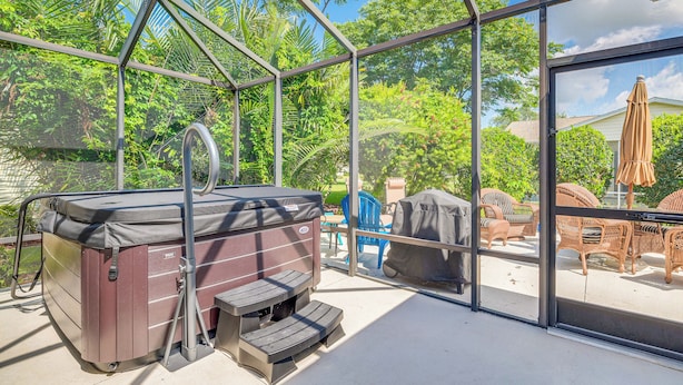 Een hottub met treden, een overdekte barbecue en rieten meubels in een afgesloten buitenruimte.