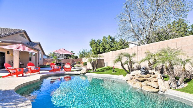 A swimming pool with red chairs and umbrellas, surrounded by a landscaped garden and a brick wall. - Family Poolside Escape 15 Mi to Dtwn Phoenix! (Avondale)