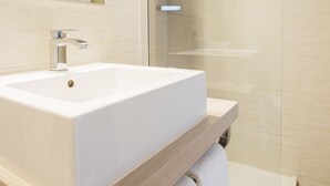 Un baño moderno con un lavamanos grande y blanco, un box de ducha de cristal y un espejo sobre el lavamanos.