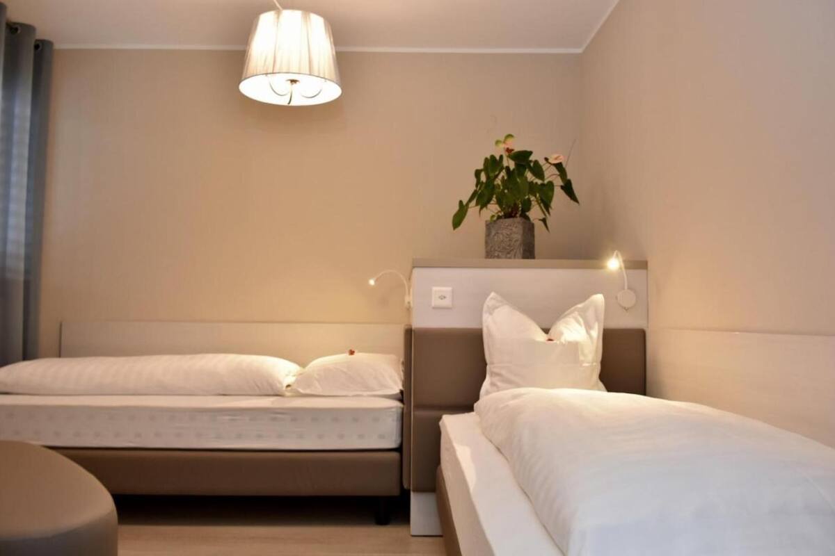 A hotel room with two beds, a bedside table, a lamp, and a potted plant.