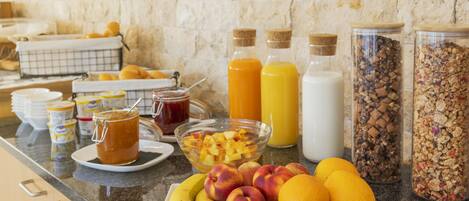A breakfast buffet with fruits, cereals, and beverages on a granite countertop.